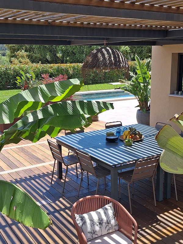 Un espace repas ombragé sous une grande pergola Terrasse avec table de repas carrée couverte par une pergola bois et acier