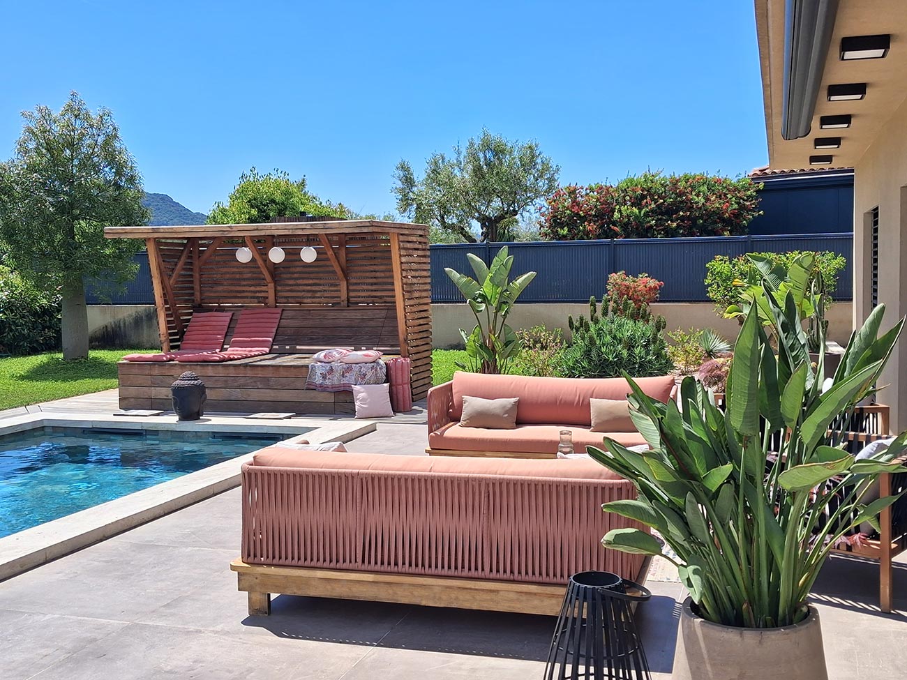 Terrasse en bord de piscine Une terrasse au bord d'une piscine avec salon de jardin rouge clair et ombrière en bois