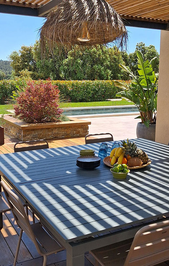 Espace repas sous une grande pergola en bois Table de repas carrée avec vue vers jardin et piscine